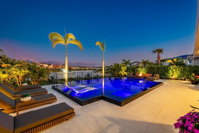 pool at dusk featuring a patio area, a water view, and a hot tub