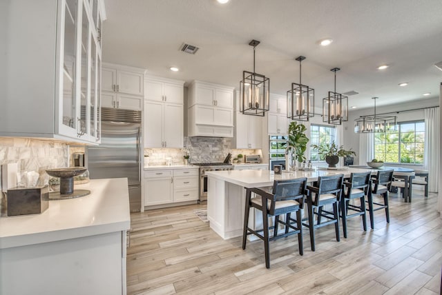 kitchen featuring high end appliances, a kitchen breakfast bar, white cabinets, and a kitchen island with sink