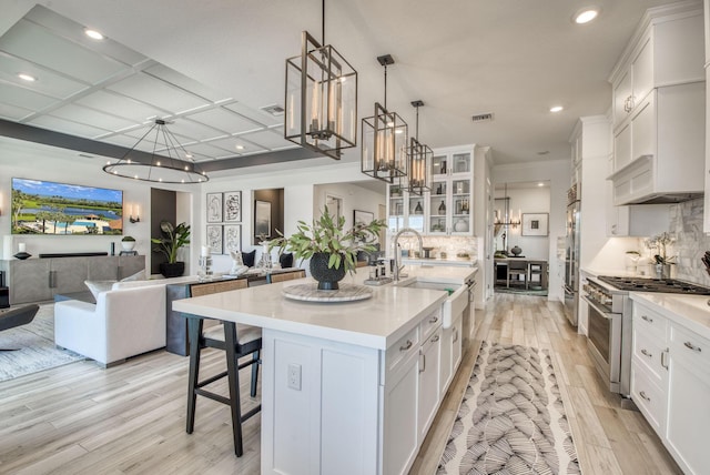 kitchen featuring decorative light fixtures, white cabinetry, a kitchen island with sink, a breakfast bar area, and high quality appliances