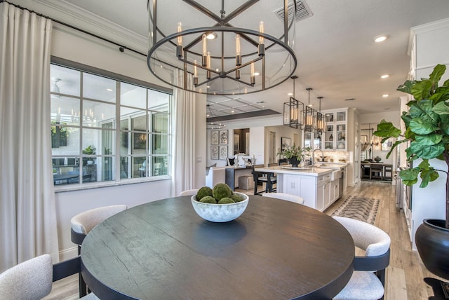 dining space with light wood-type flooring, an inviting chandelier, ornamental molding, and a wealth of natural light