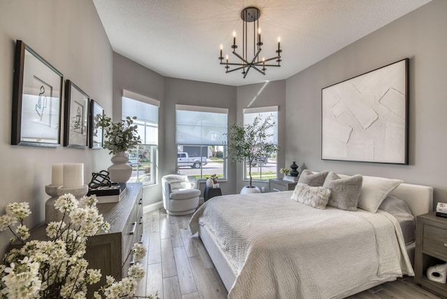 bedroom with a textured ceiling, an inviting chandelier, multiple windows, and hardwood / wood-style flooring