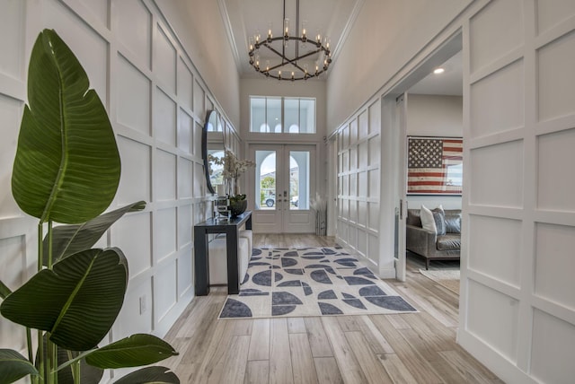 foyer with a notable chandelier, a towering ceiling, light wood-type flooring, ornamental molding, and french doors