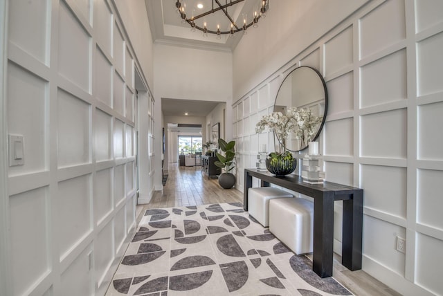 hallway with light hardwood / wood-style floors, a high ceiling, crown molding, and a notable chandelier