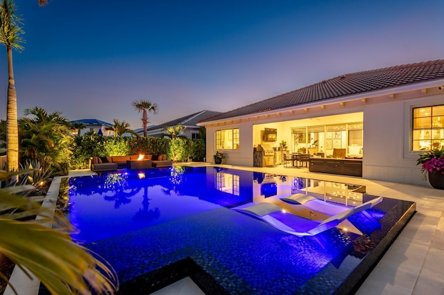 pool at dusk featuring an outdoor kitchen and a patio