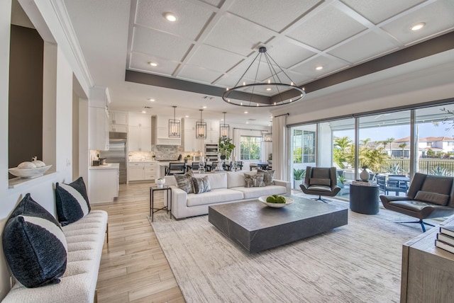 living room featuring an inviting chandelier, ornamental molding, and coffered ceiling