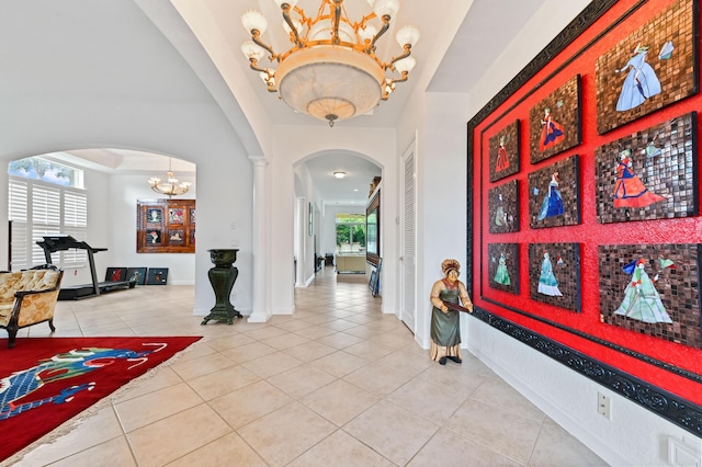 foyer entrance with decorative columns, a tray ceiling, tile patterned floors, and a chandelier