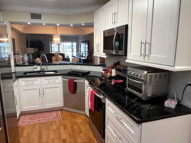 kitchen with sink, appliances with stainless steel finishes, a chandelier, white cabinets, and light wood-type flooring