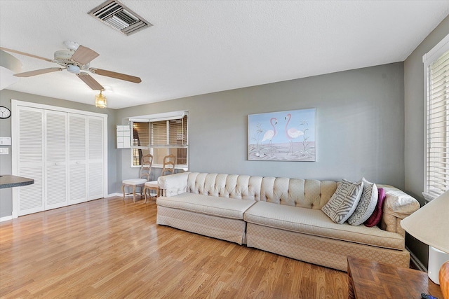 living room with ceiling fan, a textured ceiling, and light hardwood / wood-style flooring