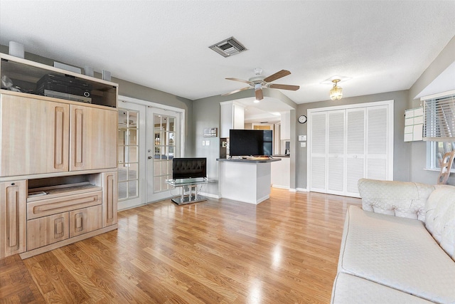 living room with a textured ceiling, ceiling fan, light hardwood / wood-style floors, and french doors