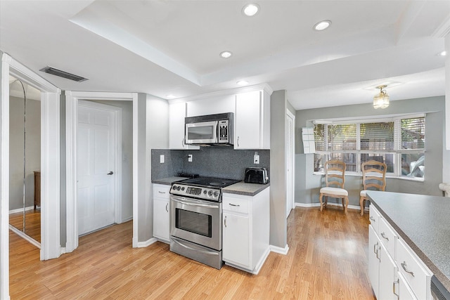 kitchen featuring white cabinets, stainless steel appliances, light hardwood / wood-style floors, backsplash, and a tray ceiling