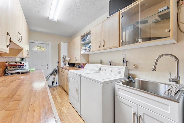 washroom with washer and dryer, light wood-type flooring, a textured ceiling, cabinets, and sink