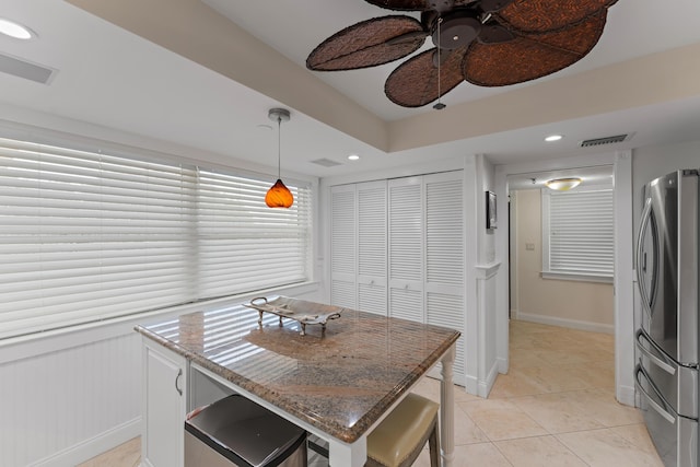 kitchen featuring ceiling fan, light tile patterned floors, hanging light fixtures, light stone countertops, and stainless steel fridge