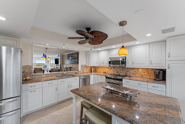 kitchen featuring stainless steel appliances, white cabinetry, a tray ceiling, hanging light fixtures, and a breakfast bar