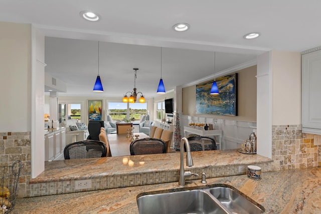 kitchen featuring ornamental molding, pendant lighting, light stone counters, sink, and an inviting chandelier