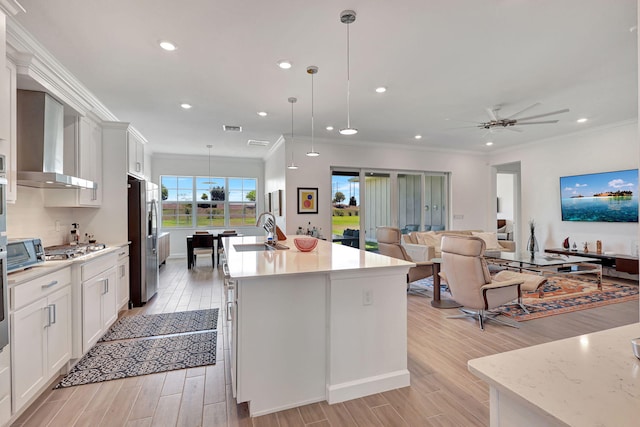 kitchen with pendant lighting, appliances with stainless steel finishes, wall chimney range hood, white cabinetry, and sink