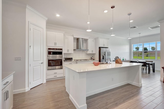 kitchen featuring an island with sink, white cabinets, wall chimney range hood, and hanging light fixtures