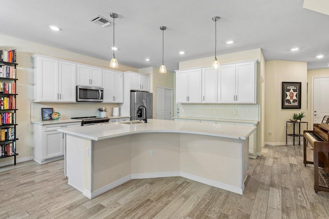 kitchen with decorative light fixtures, stainless steel appliances, a center island with sink, light wood-type flooring, and white cabinets