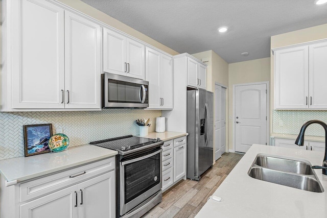 kitchen with a textured ceiling, decorative backsplash, white cabinets, appliances with stainless steel finishes, and sink