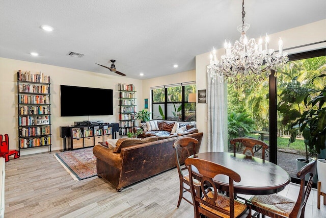 dining room with ceiling fan with notable chandelier, a textured ceiling, and light hardwood / wood-style flooring