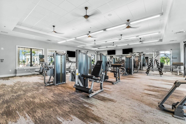 gym featuring a raised ceiling, ceiling fan, and carpet