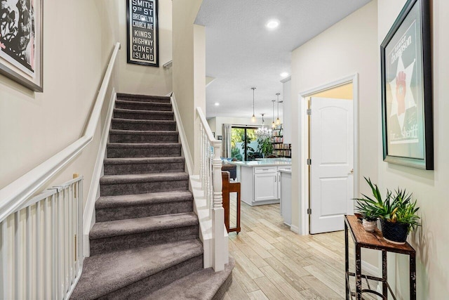 stairway featuring an inviting chandelier, a textured ceiling, and hardwood / wood-style floors