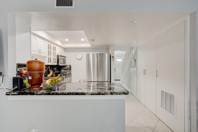 kitchen with kitchen peninsula, stainless steel appliances, a raised ceiling, white cabinets, and light tile patterned flooring