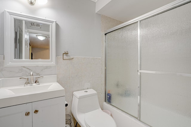 full bathroom featuring toilet, shower / bath combination with glass door, tile walls, and vanity