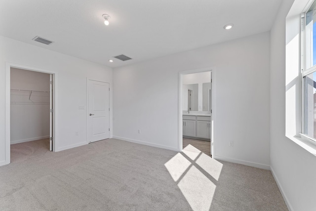 unfurnished bedroom featuring a walk in closet, a closet, ensuite bath, and light colored carpet