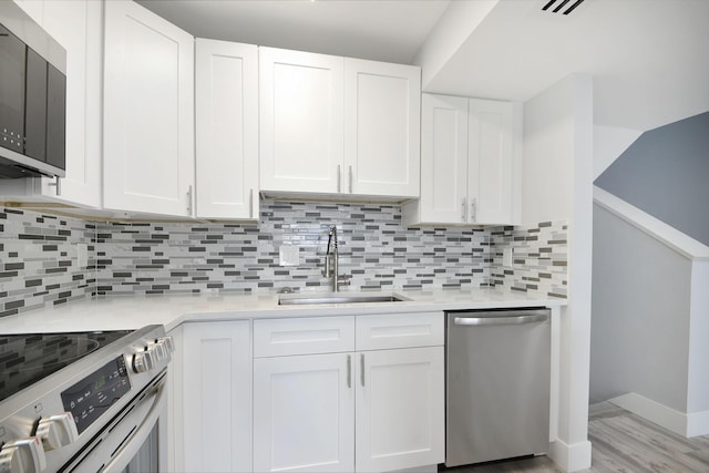 kitchen featuring stainless steel appliances, sink, light hardwood / wood-style flooring, white cabinetry, and backsplash