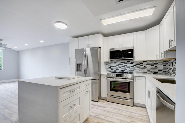 kitchen with light hardwood / wood-style flooring, a kitchen island, backsplash, white cabinets, and appliances with stainless steel finishes