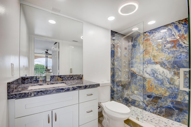 bathroom with toilet, tiled shower, and vanity