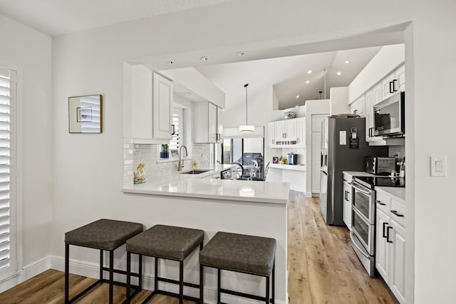 kitchen with tasteful backsplash, decorative light fixtures, kitchen peninsula, appliances with stainless steel finishes, and white cabinets