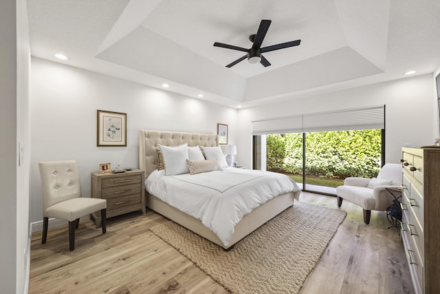 bedroom with a raised ceiling, light hardwood / wood-style flooring, access to outside, and ceiling fan