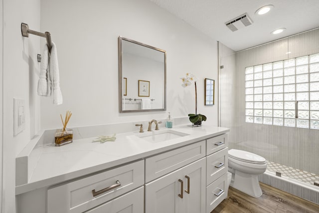 bathroom with toilet, vanity, wood-type flooring, a textured ceiling, and a tile shower