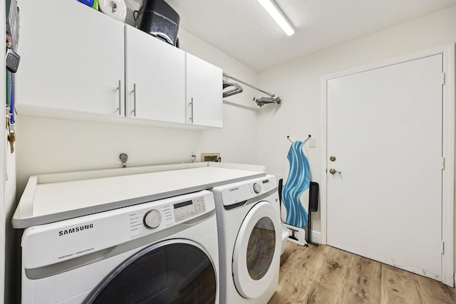 washroom with light wood-type flooring, washing machine and dryer, a textured ceiling, and cabinets