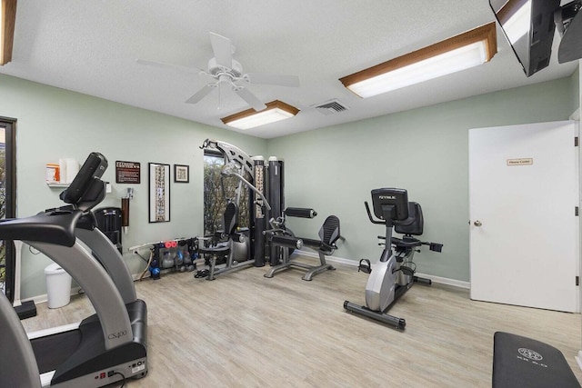 workout room with light wood-type flooring, ceiling fan, and a textured ceiling