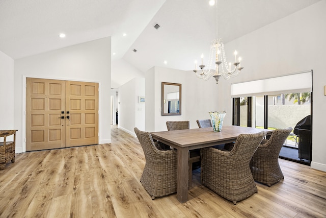 dining space with high vaulted ceiling, an inviting chandelier, and light hardwood / wood-style floors