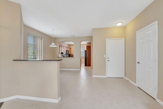 kitchen with light tile patterned floors, kitchen peninsula, dark stone counters, and decorative light fixtures