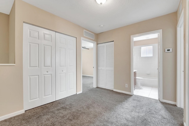 unfurnished bedroom featuring multiple closets, carpet, and ensuite bath