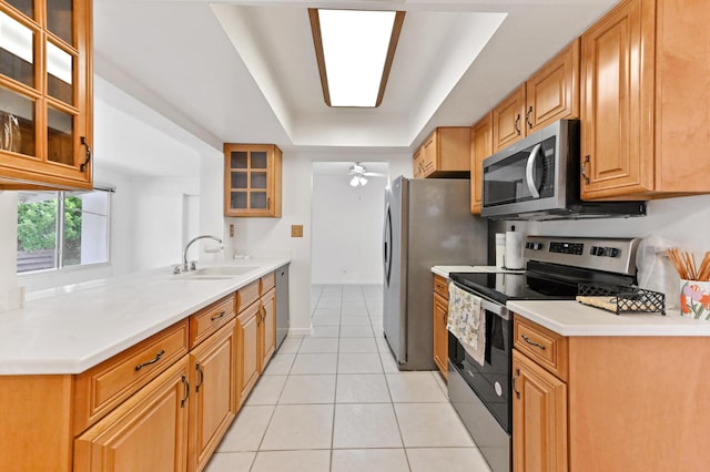 kitchen with light tile patterned flooring, a sink, a ceiling fan, appliances with stainless steel finishes, and a tray ceiling