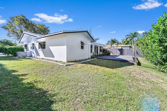 view of side of home featuring a lawn, a patio area, fence, and stucco siding