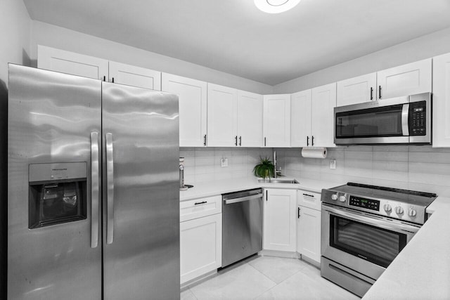 kitchen with light tile patterned floors, appliances with stainless steel finishes, white cabinetry, and tasteful backsplash