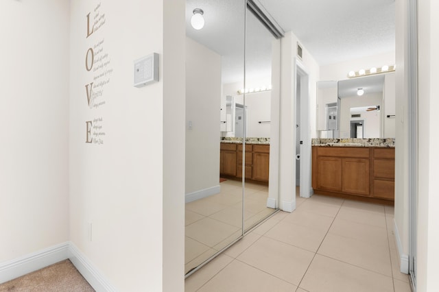 hall with sink, a textured ceiling, and light tile patterned flooring