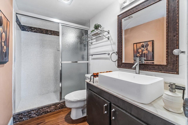 bathroom with wood-type flooring, vanity, toilet, and a shower with door