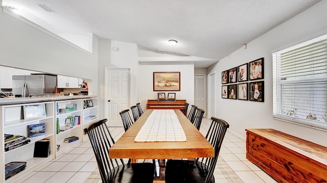 tiled dining space featuring a textured ceiling and lofted ceiling