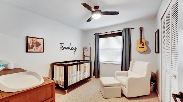 carpeted bedroom with ceiling fan, a closet, and a crib