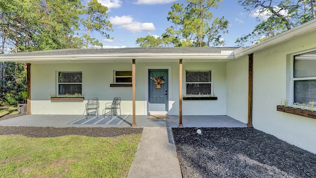 view of exterior entry featuring covered porch and a patio