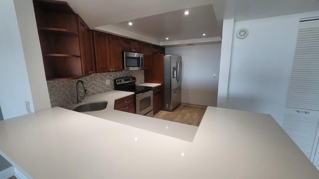 kitchen featuring kitchen peninsula, appliances with stainless steel finishes, decorative backsplash, a raised ceiling, and sink