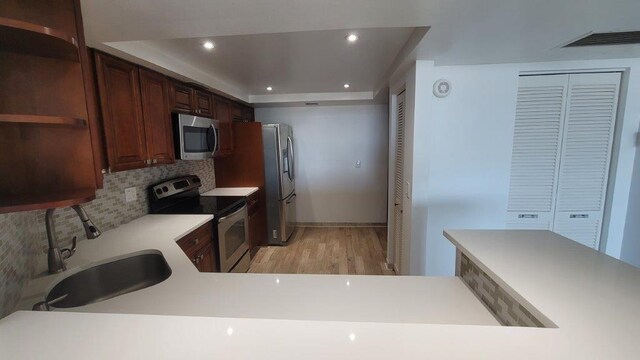 kitchen featuring stainless steel appliances, decorative backsplash, sink, a raised ceiling, and light wood-type flooring