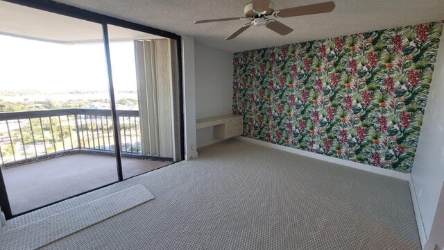 carpeted empty room featuring ceiling fan, expansive windows, and a textured ceiling